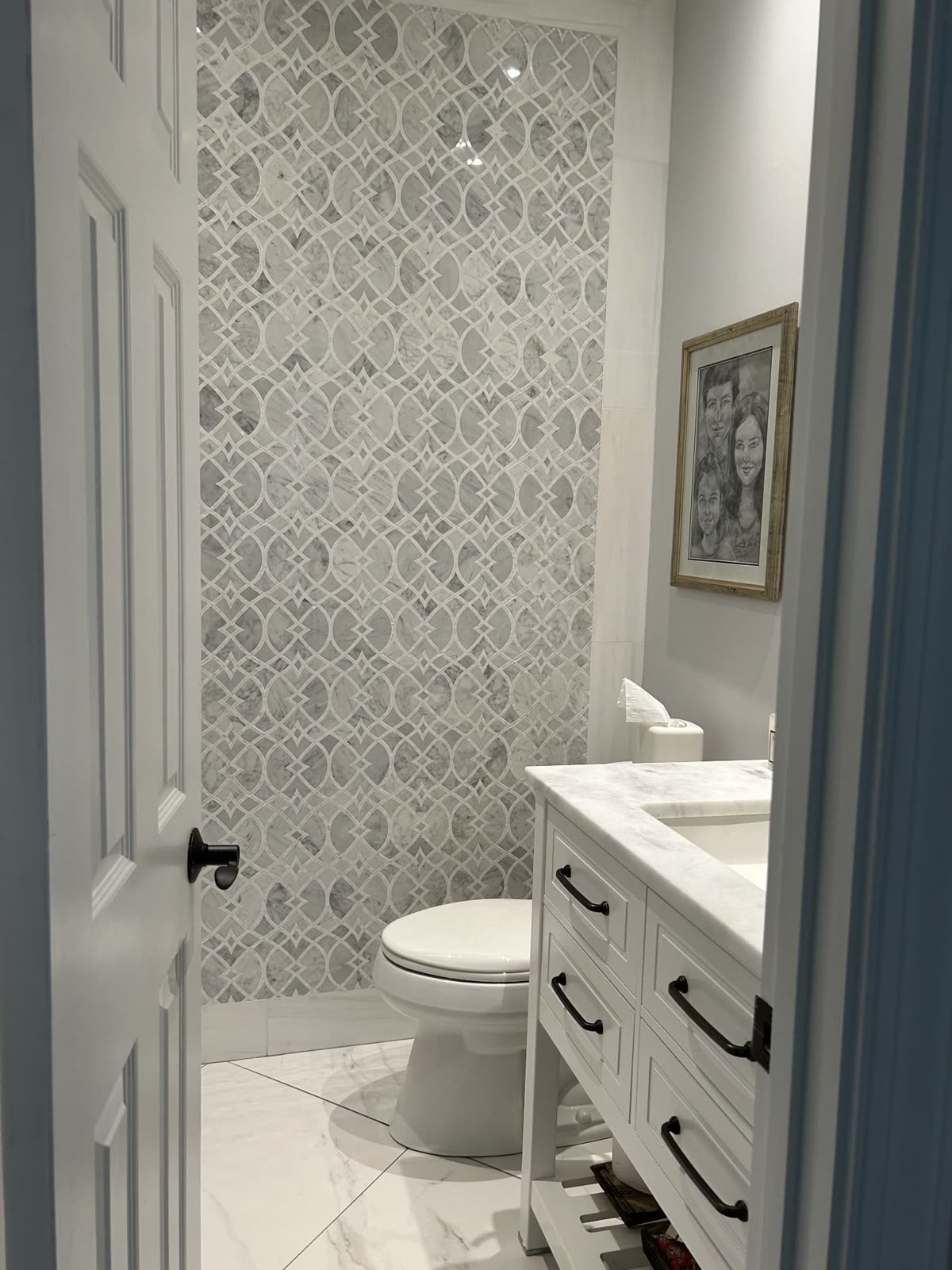 Powder room with patterned tile accent wall and white vanity