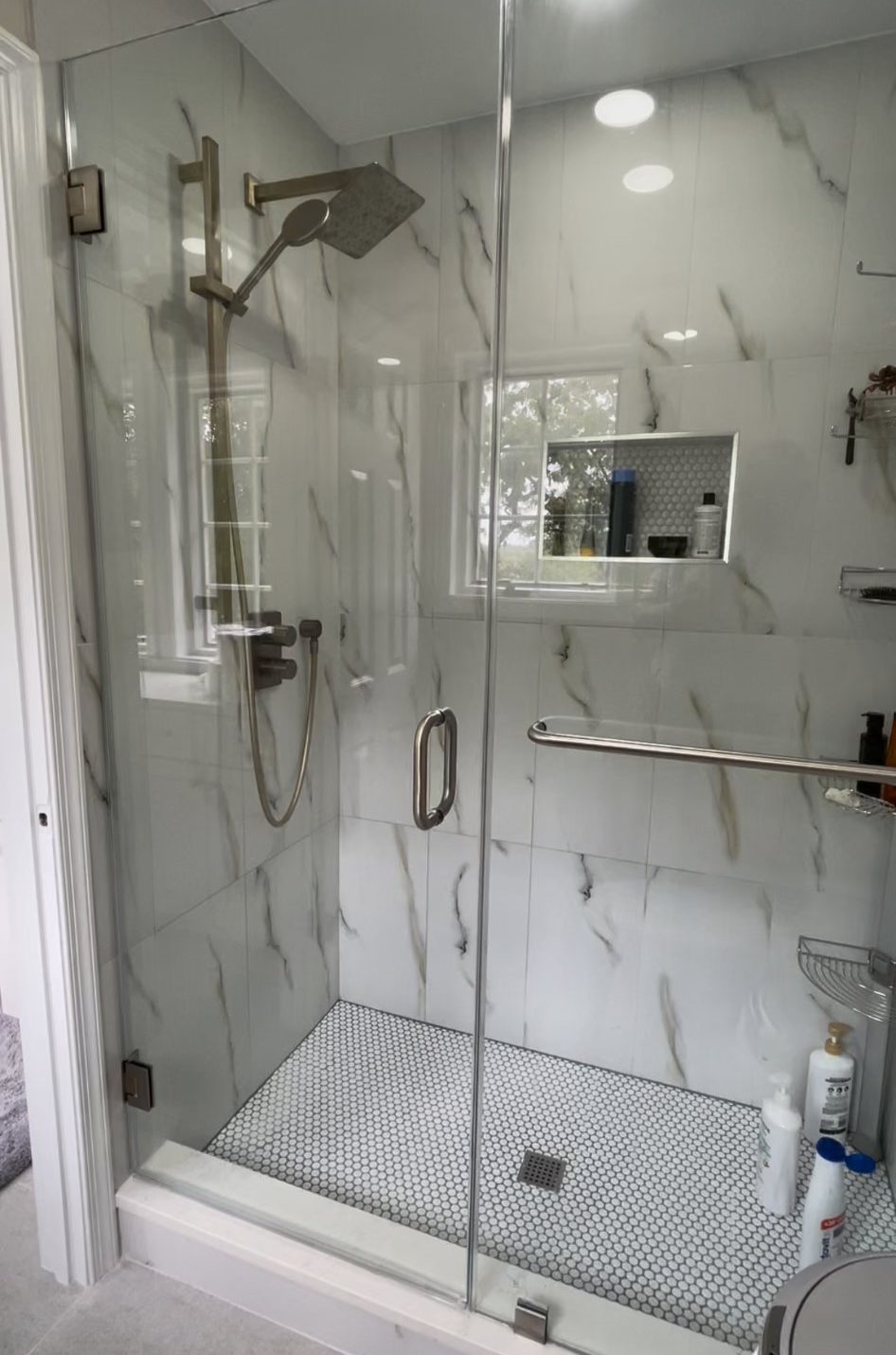 Walk-in shower with marble-look tile, glass enclosure and penny tile floor