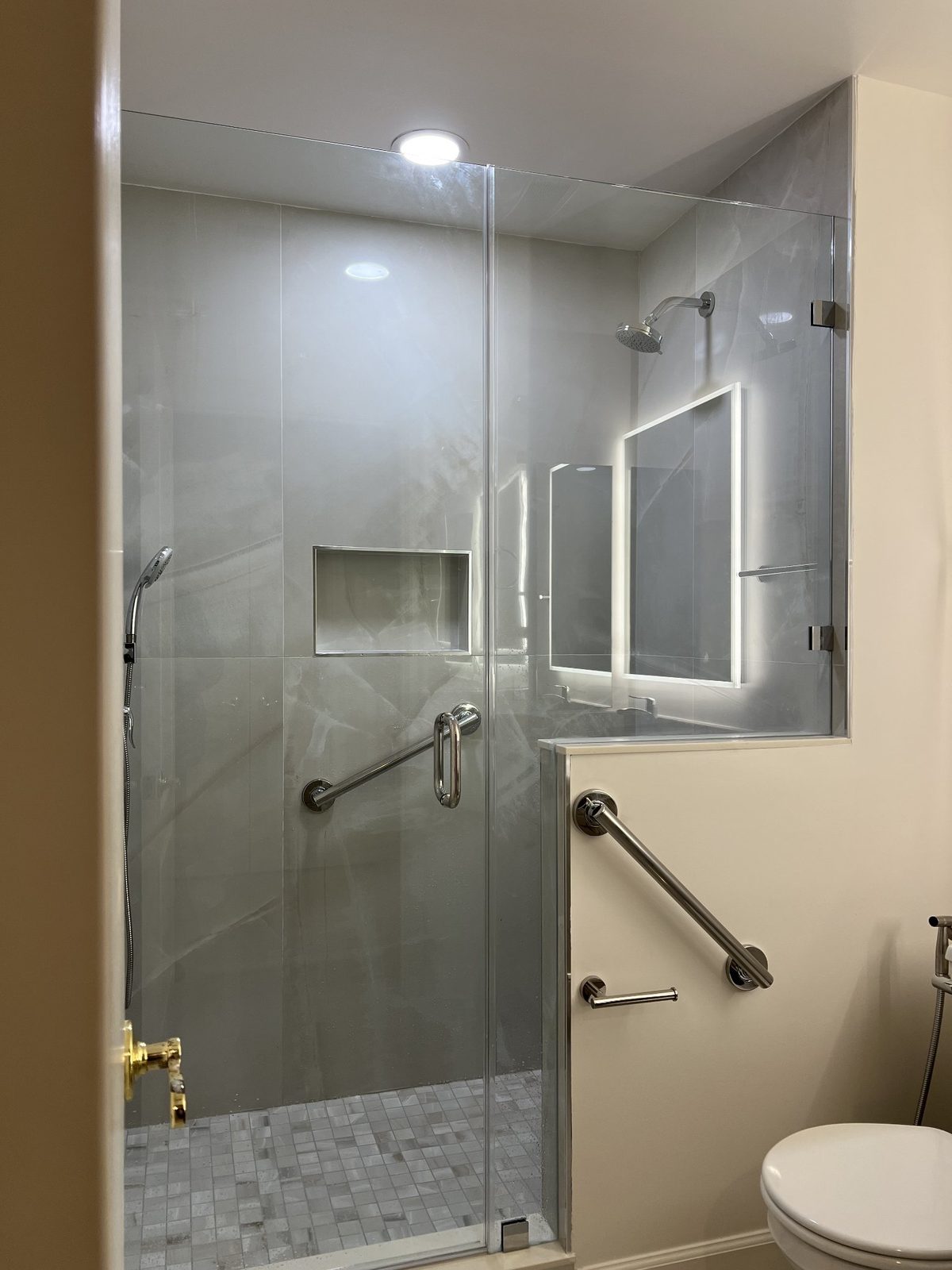 Bathroom with glass walk-in shower, gray tile walls and grab bars